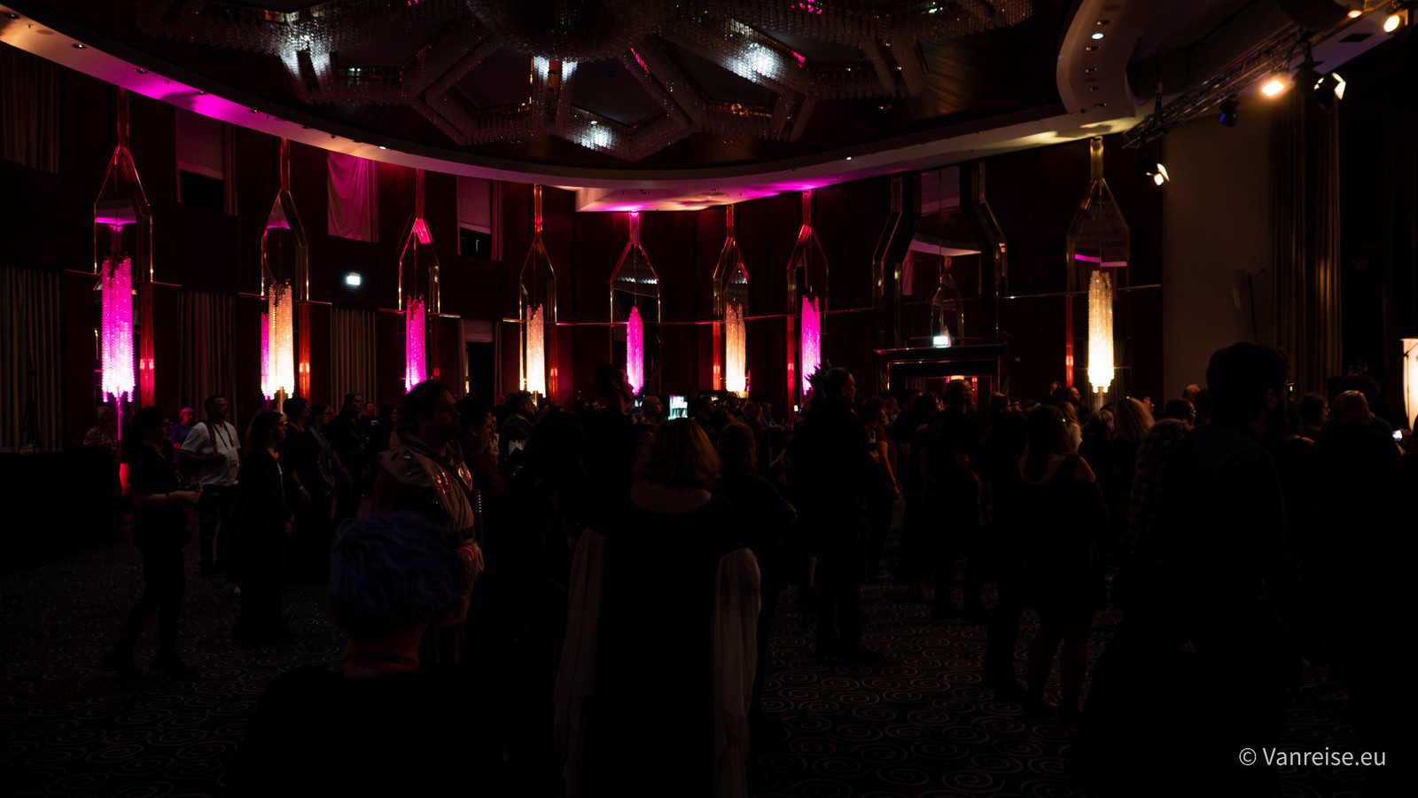 Besucher stehen im Saal mit pink und warmweiß beleuchteten Wandleuchten.