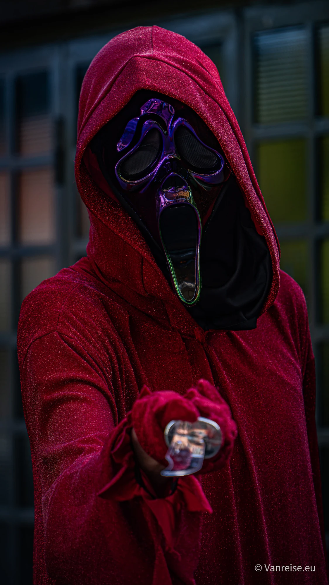 Person mit roter Kapuze und schwarzer Ghostface-Maske mit violetten Konturen.