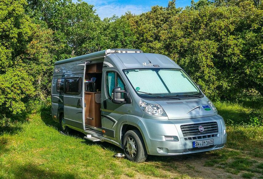 Wiese mit Bäumen und einem Ausgebauten Camping Transporter